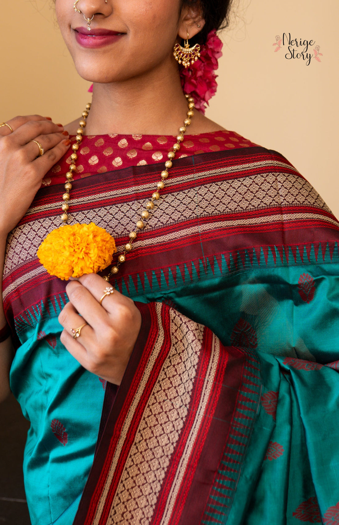 Person wearing a traditional saree with a floral accessory, on a beige background.