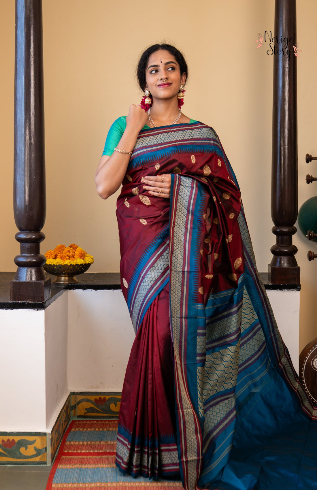 Woman wearing a traditional maroon and blue saree with a decorative border indoors.