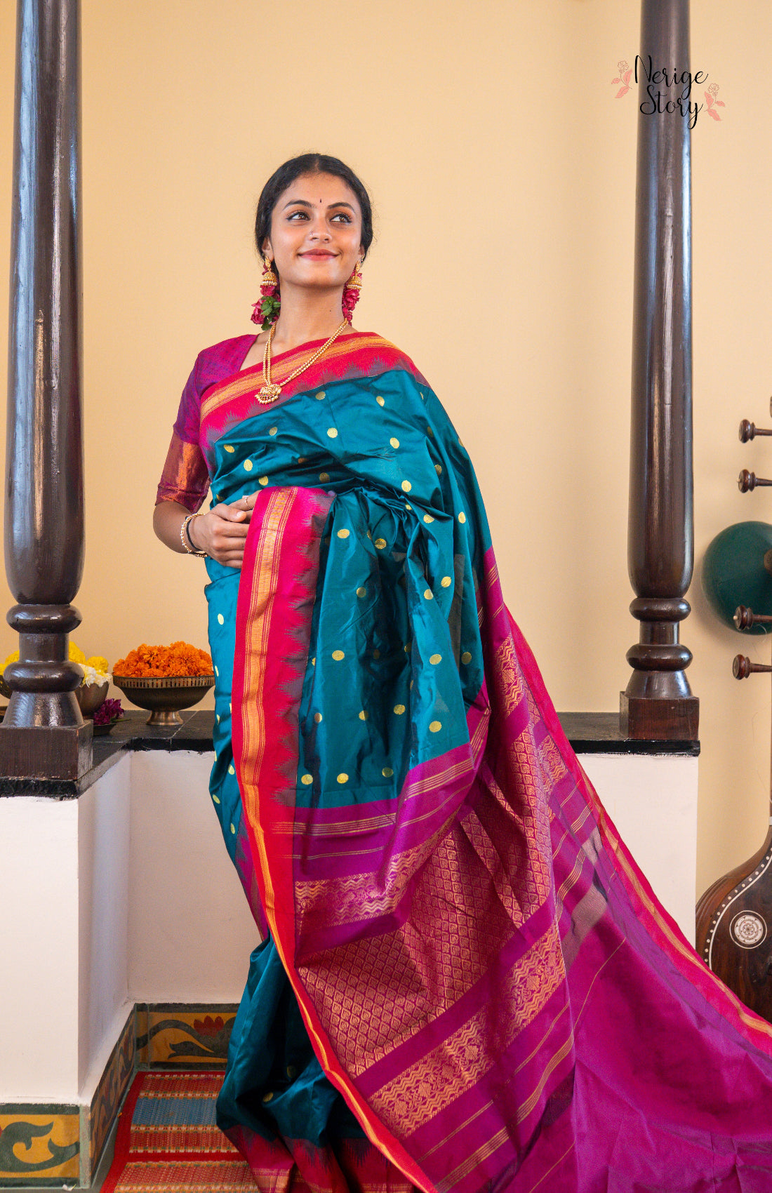 Woman wearing a traditional saree with a teal and pink design, standing indoors.